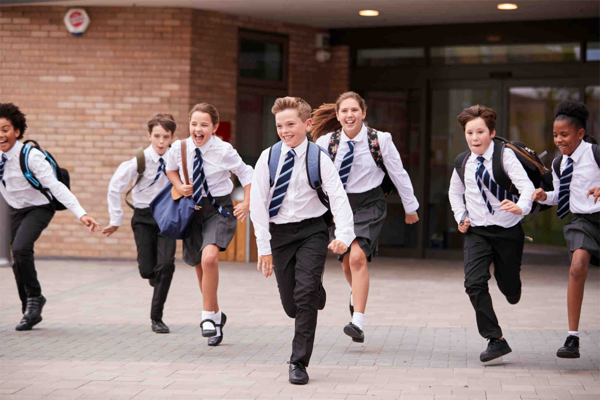 Seven children with their schoolbags in school uniform running out of school entrance looking very happy - Footsteps Educational Psychology services for schools